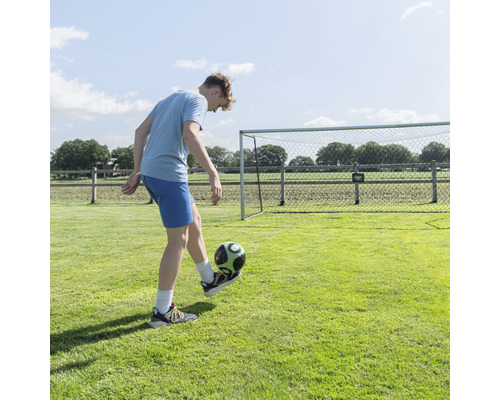 Un jeune homme joue au football devant un but de football dans le jardin