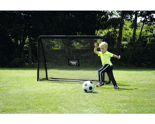 Un garçon joue au football devant un but de foot dans le jardin.