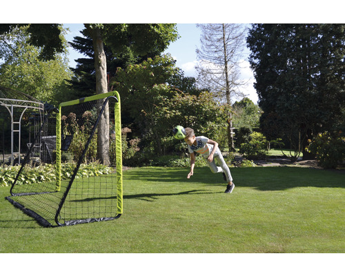 Junge köpft Fussball vor Fussballtor im Garten