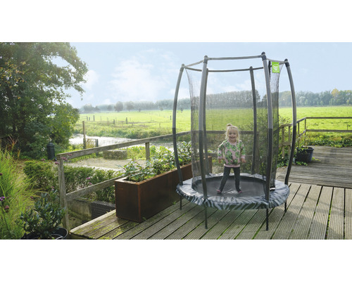 Petite fille sautant sur un trampoline de jardin rond avec filet de sécurité sur une terrasse.