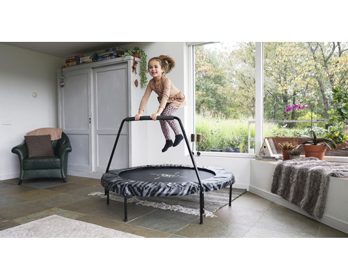 Une fille saute sur un trampoline de fitness avec une barre d''appui dans une pièce lumineuse.