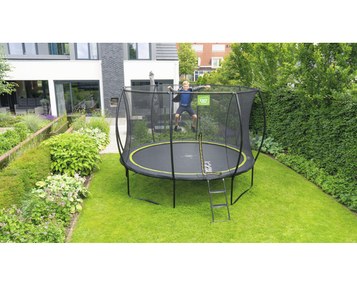 Garçon sautant sur un trampoline de jardin noir avec filet de sécurité et échelle dans le jardin.