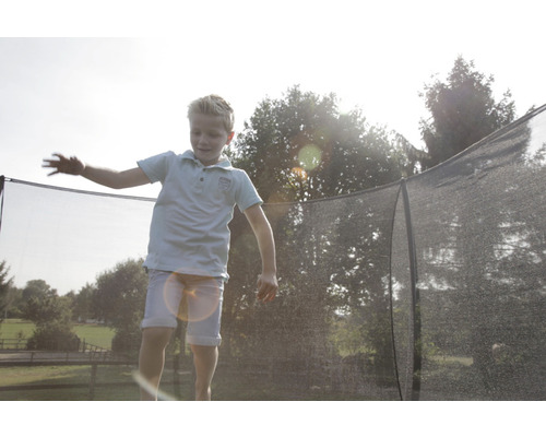 Un garçon saute sur un trampoline de jardin avec filet de sécurité.