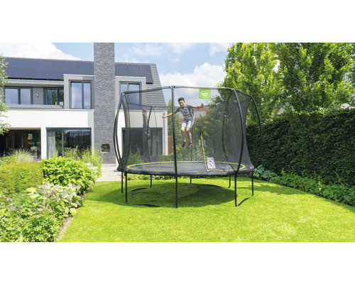 Garçon sautant sur un trampoline de jardin avec filet de sécurité devant une maison moderne