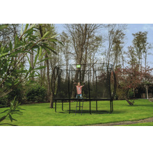Enfant sur un trampoline de jardin avec filet de sécurité et échelle dans le jardin.