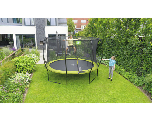 Trampoline de jardin rond avec filet de sécurité, sur lequel un enfant saute et un autre se tient à côté