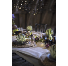 Festlich gedeckter Tisch mit Kugelleuchten, Geschirr, Gläsern und saisonalem Gemüse als Dekoration.