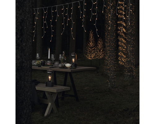 Dekorierte Gartenszene mit Lichterketten, Tisch, Sitzbank und Lampen für eine stimmungsvolle Atmosphäre.