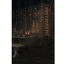 Gartenszene mit beleuchtetem Tisch, Lichterketten und Baumbeleuchtung.