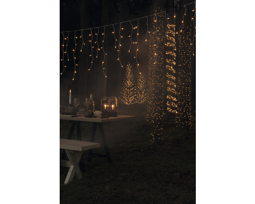 Gartenszene mit beleuchtetem Tisch, Lichterketten und Baumbeleuchtung.