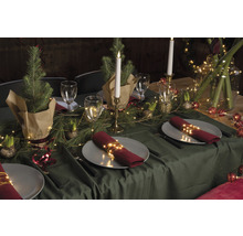 Table festive avec vaisselle, verres, bougies, branches de sapin et guirlandes lumineuses comme décoration.
