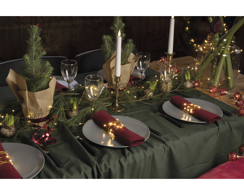 Table festive avec vaisselle, verres, bougies, branches de sapin et guirlandes lumineuses comme décoration.