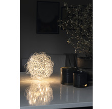 Dekorative Kugel-Tischleuchte neben Kerzen und Topfpflanze auf Tisch