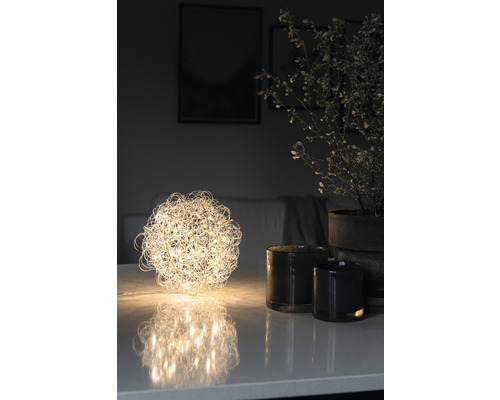 Dekorative Kugel-Tischleuchte neben Kerzen und Topfpflanze auf Tisch