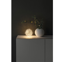 Dekoratives Arrangement mit einer leuchtenden Drahtkugel, einer Vase und Zweigen auf einem Schrank.