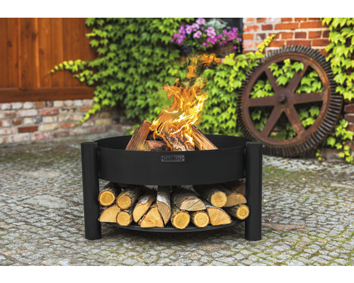 Schwarze Feuerschale mit Holz und brennendem Feuer im Garten