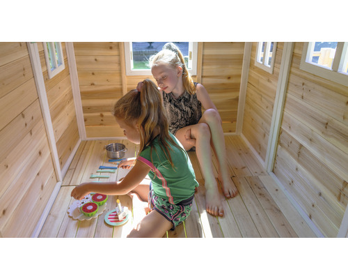 Zwei Kinder spielen in einem Holzspielhaus mit Fenstern und Spielzeuggeschirr.