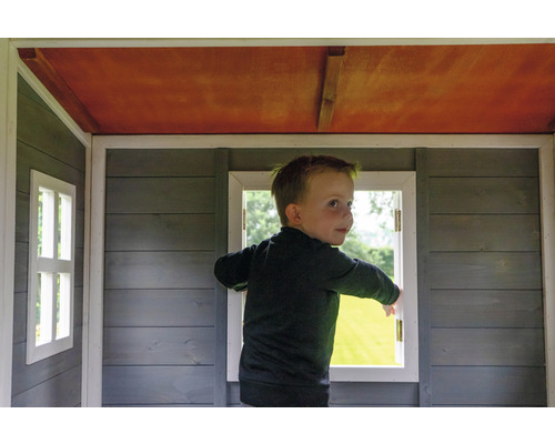 Ein Kind steht in einem Holzspielhaus mit Fenstern