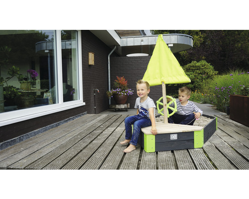 Bac à sable en forme de bateau avec voile et deux enfants jouant dans le jardin.