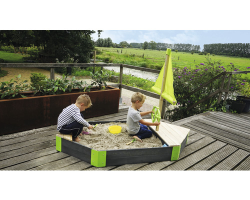 Bac à sable en forme de bateau avec deux enfants jouant dans le jardin.