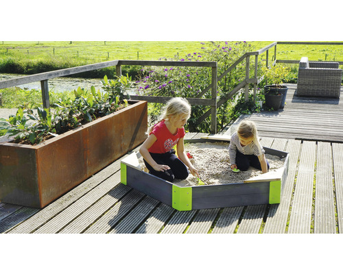 Deux enfants jouent dans un bac à sable sur une terrasse en bois à côté d''une jardinière.