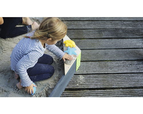 Fille jouant dans un bac à sable avec des jouets de sable sur une terrasse en bois