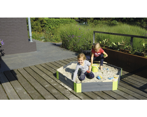 Deux enfants jouent dans un bac à sable en bois dans le jardin.