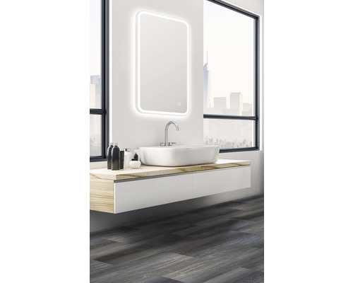 Badezimmer mit beleuchtetem Spiegel, Waschbecken und Unterschrank vor einem Fenster.