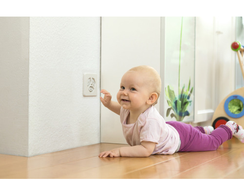 Baby krabbelt auf Holzboden und berührt Steckdosensicherung
