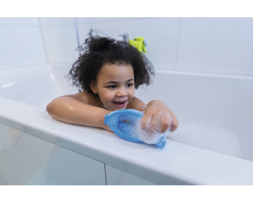 Un enfant joue dans une baignoire avec de la mousse de bain et un jouet de bain.