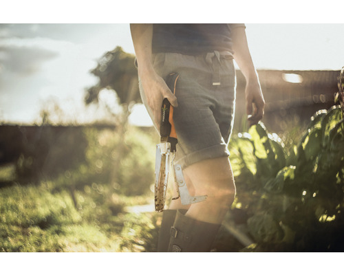 Une personne tient un désherbeur Fiskars usagé dans le jardin