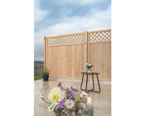 Scène de jardin avec clôture en bois, petite table et compositions florales.