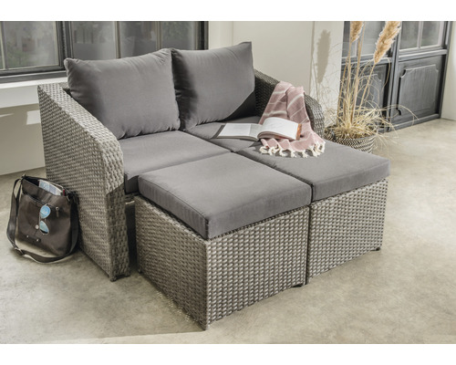 Graue Loungeecke aus Rattan mit Kissen und Fußhockern auf einer Terrasse