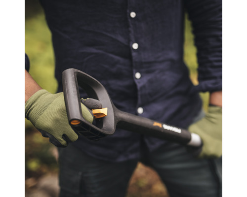 Une personne tient une bêche Fiskars noire avec une poignée et une lame, tout en portant des gants.