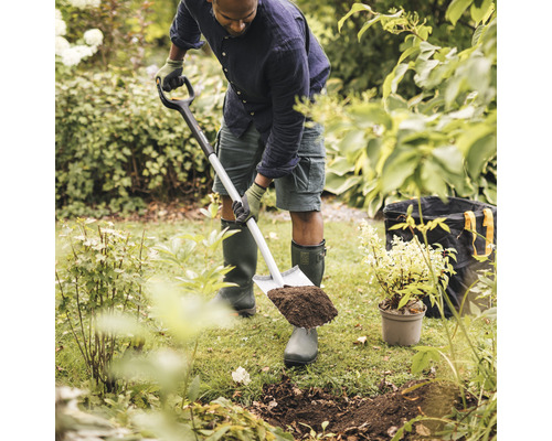 Un homme creuse un trou dans le jardin avec une bêche.