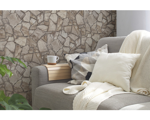 Salon avec mur en pierre, canapé, coussins, couverture et tasse