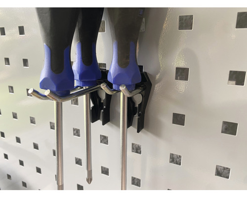 Deux tournevis sont suspendus à un support mural perforé.