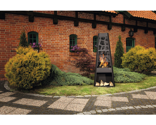 Cheminée de jardin noire avec bûches de bois devant un bâtiment en briques