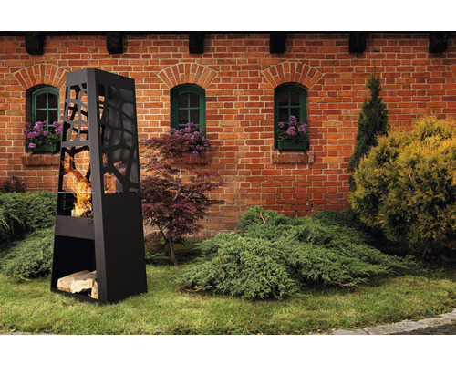 Brasero de terrasse décoratif en métal avec rangement pour le bois devant un bâtiment en briques