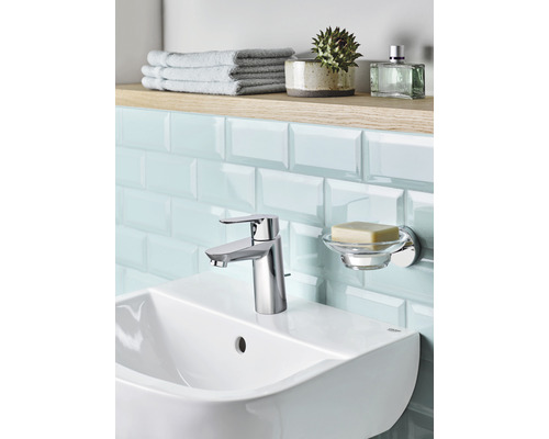 Lavabo de salle de bain avec robinet, porte-savon, serviettes et accessoires sur une étagère