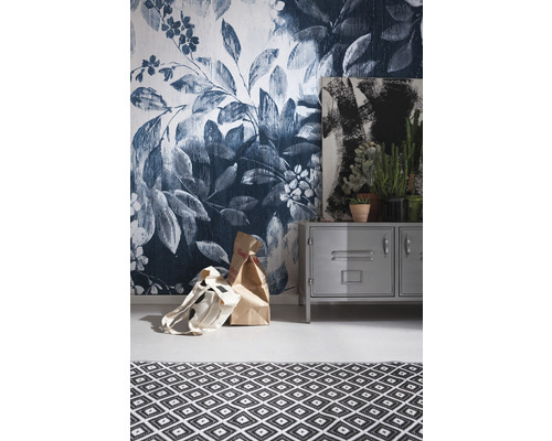 Raumansicht mit Blumentapete, Metallschrank, Gemälde, Zimmerpflanzen und Teppich mit geometrischem Muster