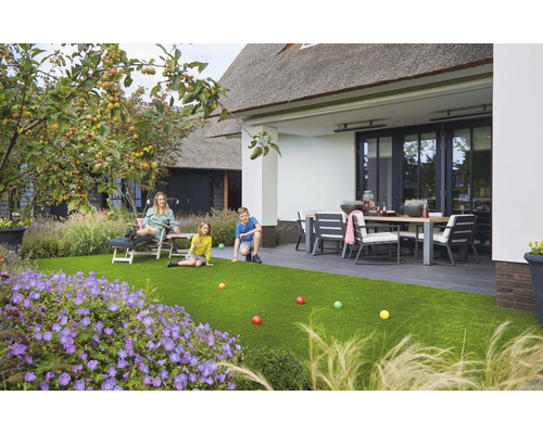 Famille se détend sur du gazon synthétique dans le jardin avec terrasse et mobilier de jardin