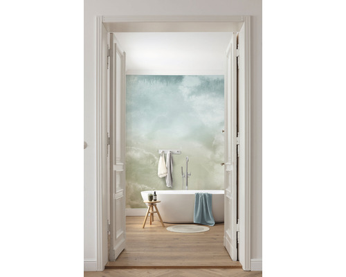 Salle de bains lumineuse avec baignoire, tabouret et papier peint à motifs de nuages, vue à travers une porte ouverte.