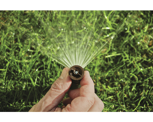 Une main tient un arroseur de pelouse qui pulvérise de l''eau.