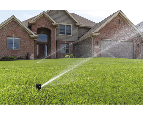 Bewässerungssystem mit Rasensprengern vor einem Haus.