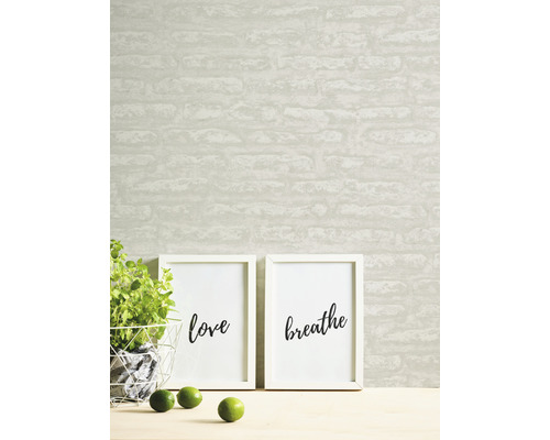 Papier peint à motif de briques, deux reproductions d''art encadrées avec les mots amour et respirer, plante en pot et citrons verts sur une table.