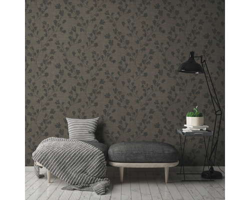 Un salon avec un papier peint à motifs, un tabouret, un fauteuil et un lampadaire.