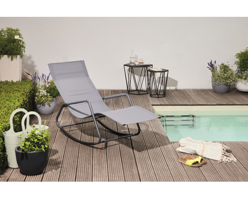 Szene mit grauer Gartenliege, zwei Beistelltischen und Pflanzen auf einer Holzterrasse neben einem Pool