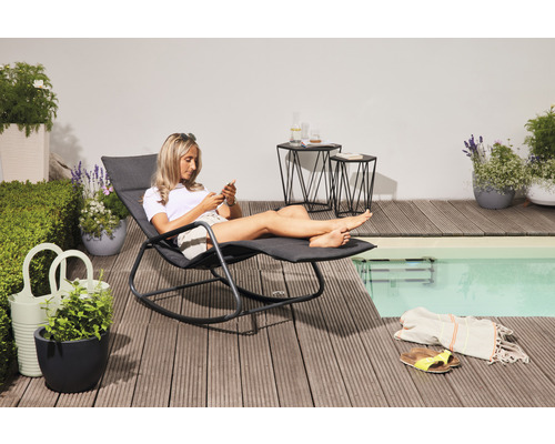 Frau entspannt auf einer Gartenliege neben einem Pool, umgeben von Beistelltischen und Pflanzgefäßen auf einer Holzterrasse.
