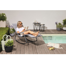 Szene im Außenbereich mit Frau, die ein Buch auf einer Gartenliege am Pool liest. Zwei Beistelltische, Pflanzen und Dekorationen vervollständigen das Bild.